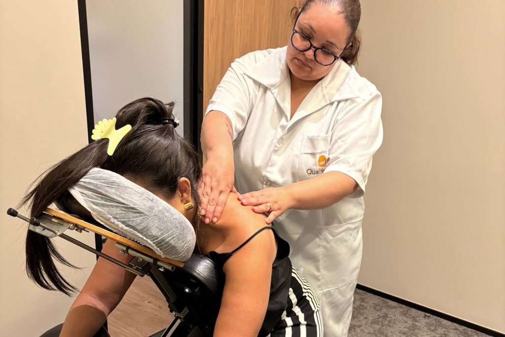 rofissional da Qualiforma realiza massagem nas costas e ombros de uma cliente acomodada em uma cadeira ergonômica de quick massage